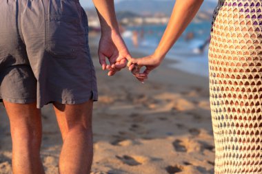 Mutlu çift el ele tutuşup deniz kıyısında birbirlerine bakıyorlar. Bir adam ve bir kadın okyanusun yakınındaki kumun üzerinde duruyorlar. Deniz kıyısında yeminler ve vaatler.