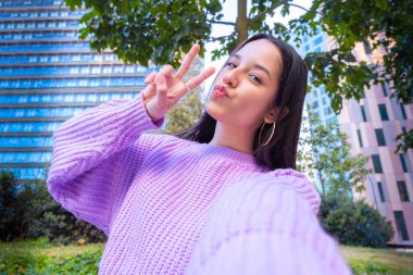 Mutlu genç Latin kadın akıllı telefonuyla selfie çekiyor barış işareti yapıyor.