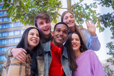 Genç gülümseyen öğrenciler bir dizüstü bilgisayarla video görüşmesi yaparlar. Dört öğrenci el sallıyor ve dışarıda gülüyor. Kavram: Üniversite hayatı.