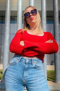 Güneş gözlüklü genç kadın şaşırmış görünüyor ve kolları kameraya çaprazlanmış..