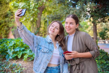 İki beyaz kadın akıllı telefonlarıyla selfie çekiyor..