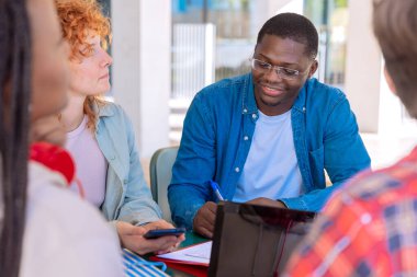Laptopları ve notları olan beş öğrenci sınavları incelemek için kampüsün yanında oturuyor. Laptoplarla kampüsün yakınında oturuyor ve iletişim kuruyorlar..