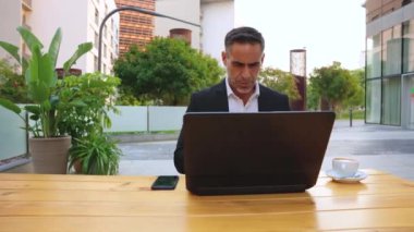 Takım elbiseli yetişkin bir adam elinde bir telefon tutuyor, mesajlar yazıyor ve internetten bir uygulama kullanarak haberleri okuyor.