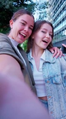  İki genç kadın dışarıda selfie çekerken keyifli bir anı paylaşıyorlar. Biri gülümsüyor, diğeri ise şaşırmış bir ifadeye sahip, günlük, dostane sahnelere heyecan katıyor..