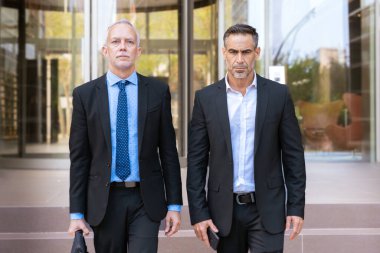 Resmi takım elbiseli iş adamları, biri kendine güvenen biri ve diğeri de ofis binasının dışındaki merdivenlerde gelişigüzel oturan biri. Modern kurumsal tarzı, güveni ve profesyonel dinamiği vurgular