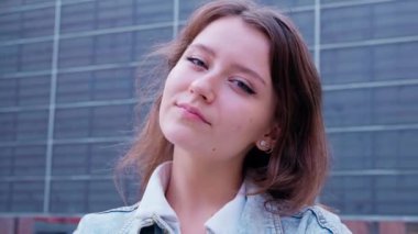 Kendine güvenen bir kadın şehir caddesinde duruyor, doğrudan kameraya bakıyor. Modern binalarla çevrili, ciddi ama dengeli bir ifadesi var. Güçlendirme ve kendine güven kavramı.