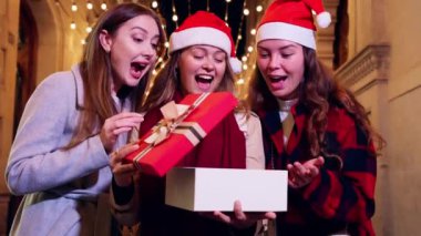 Noel Baba şapkalı üç neşeli kadın bir bayram akşamında Noel hediyesi kutularını açarken şaşırıp heyecanlanıyorlar. Şehir ışıkları ve dekorasyonları şu ana büyülü bir atmosfer katıyor..