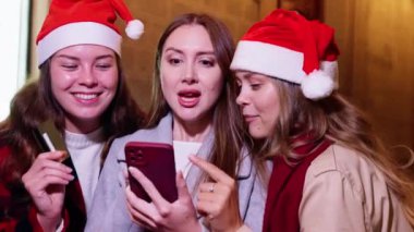 Bir şehir merkezinde elinde kredi kartı ve telefonla gülümseyen ve etkileşime geçen üç genç kadın. Bir alışveriş anının tadını çıkarıyorlar, parlak bir günde mutluluk ve heyecanı yansıtıyorlar. 