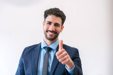 Takım elbiseli profesyonel bir genç adam sıcak bir şekilde gülümsüyor ve onaylıyor. Temiz ve parlak arka plan, bir işletme veya şirket ortamında güven, pozitiflik ve başarıyı vurgular.