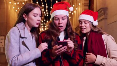 Bir şehir merkezinde elinde kredi kartı ve telefonla gülümseyen ve etkileşime geçen üç genç kadın. Bir alışveriş anının tadını çıkarıyorlar, parlak bir günde mutluluk ve heyecanı yansıtıyorlar. 