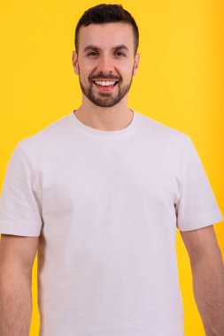 Beyaz gömlek giyen neşeli bir adam parlak sarı bir arka plana sıcak bir şekilde gülümsüyor. Canlı ve minimalist ortam bu resmi yaşam tarzı, günlük portreler ve pozitif temalar için ideal kılıyor..