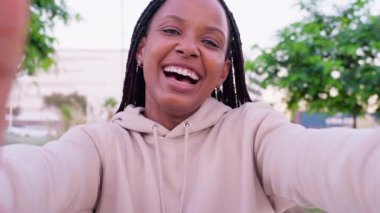  Genç bir kadın, açık havada sarı bir klasörü tutarken selfie çekerken ışıl ışıl gülümsüyor. Gözlük takıyor ve sıradan bir kot ceket giyiyor. Arka planda çitleri ve yeşilliği olan güneşli bir gün var..