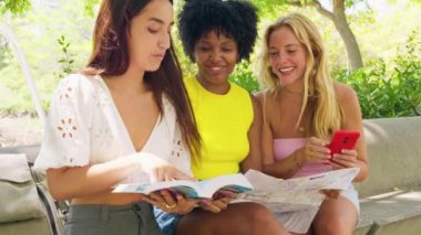 Üç neşeli kadından oluşan bir grup, açık hava ortamında gezmek ve gülümsemek için bir harita kullanıyor. Yolculuk, macera ve dostluk temaları için mükemmel. Canlı ve güneşli yaz atmosferleri..