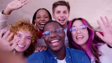  Mutlu bir grup genç arkadaş doğal bir ortamda selfie çekiyorlar. Çok çeşitliler, gülümsüyorlar ve kameraya el sallıyorlar. Güneşli gökyüzünün altında neşe ve dostluk saçıyorlar.. 
