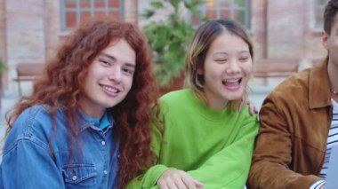 Grup öğrencileri açık hava ortamında gülümsüyor ve birbirlerine sarılıyorlar. Neşeli ifadeleri ve sıcak yoldaşlıkları rahat bir ortamda dostluk ve mutluluğu yansıtıyor..