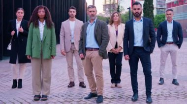 Modern ofis ortamında yedi farklı iş adamı bir arada duruyor. Profesyonel giysiler içinde takım çalışması ve kapsama gösteriyorlar. Kameraya dostça ifadelerle bakıyorlar.