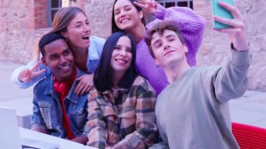 Grup Bir grup neşeli arkadaş bir selfie için poz veriyor, gülümsüyor ve şakacı hareketler yapıyor dışarıda tuğla duvarın yanında otururken..