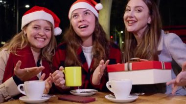 Noel Baba şapkası takan üç arkadaş açık bir kafede şenlikli içkilerin ve kahkahaların keyfini çıkarıyorlar. Birisi bir hediye kutusu tutuyor ve gece neşeli bir tatil ortamı yaratıyor. Açık Cafe 'de Noel' i kutluyoruz.. 