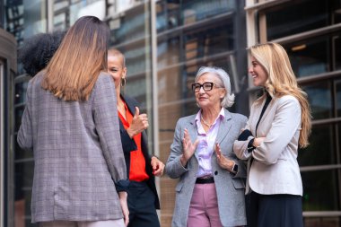 Modern bir ofis binasının önünde birlikte gülen şık iş kıyafetleri içinde neşeli, profesyonel bir kadın grubu. Kurumsal bir ortamda çeşitliliği, takım çalışmasını ve başarıyı kutlamak. 