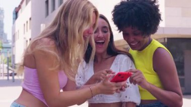 Üç genç kadın açık hava basamaklarında birlikte oturup pembe akıllı telefonlarıyla selfie çekerken gülümsüyorlar. Günlük yaz kıyafetleri giyiyorlar ve etrafları yeşilliklerle çevrili. Açık havada selfie çekiyorum..