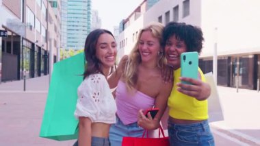 Üç kadın. Üç neşeli genç kadın, alışveriş torbalarını şehir dışında tutarken selfie çekiyorlar. Neşeli bir şekilde gülümserler, birlikte eğlenceli ve hayat dolu bir anın tadını çıkarırlar.