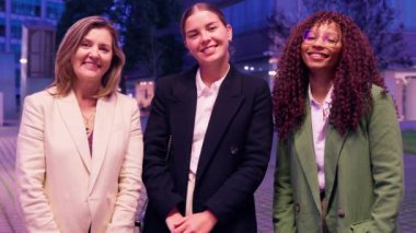 İş kıyafeti giymiş üç kadın kollarını kavuşturmuş, gülümsüyor ve modern ofis ortamında etkileşime giriyorlar. Modern bir ofis ortamında gülümseyen güven ve yoldaşlık kadınları yayarlar..