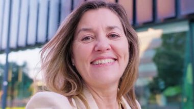 Neşeli genç bir kadının portresi, yüksek binalar ve canlı mimariyle modern şehir ortamında güvenle gülümsüyor..