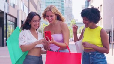 Üç genç kadın açık hava basamaklarında birlikte oturup pembe akıllı telefonlarıyla selfie çekerken gülümsüyorlar. Günlük yaz kıyafetleri giyiyorlar ve etrafları yeşilliklerle çevrili. Açık havada selfie çekiyorum..