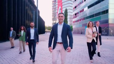 İş dünyasından profesyonellerden oluşan kendine güvenen bir grup resmi giyinmiş, takım çalışmasını, liderliği ve başarıyı temsil eden kentsel bir ortamda güvenle yürüyor.