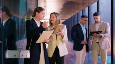 Modern bir ofis koridorunda tablet ve not defterleriyle birlikte çalışan iş dünyasından resmi giyinmiş profesyonellerden oluşan Prodüksiyon Ekibi, teknoloji ve işbirliğini vurguladı