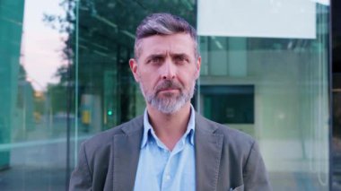 Neşeli genç bir adamın portresi, yüksek binalar ve canlı mimari ile modern bir şehir ortamında güvenle gülümsüyor..