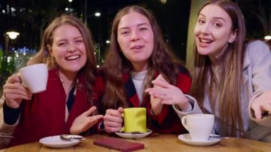 Açık bir kafede oturan üç mutlu arkadaş ellerinde fincanlarla kameraya sımsıkı gülümsüyorlar. Şehir ışıkları altında içkiler ve kahkahalarla eğlenceli ve rahat bir akşam..