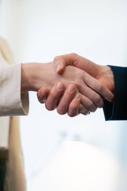 İş kıyafetleri giyen iki kişi arasındaki profesyonel el sıkışma, ortaklığı, anlaşmayı ya da bir ofis ortamındaki işbirliğini sembolize ediyor.