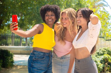 Üç genç kadın dışarıda oturuyor, gülümsüyor ve birlikte eğlenceli bir selfie çekiyorlar. Arkadaşlık, mutluluk, sosyal medya ve açık hava yaşam tarzı gibi kavramlar için mükemmel..