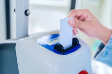 Toplu taşıma makinesine bilet sokan bir elin yakın çekimi. Elektronik cihaz giriş biletini tarıyor. Modern banliyö ve ulaşım sistemi kavramı.