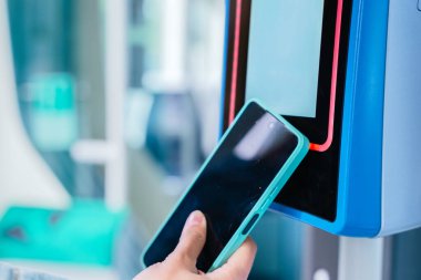 Bir toplu taşıma bileti onaylayıcısına ulaşılamayacak bir ödeme için akıllı telefon kullanan bir elin yakın çekimi. Kentsel bir ortamda modern ve uygun bir dijital işlem.