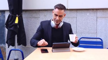 Siyah takım elbiseli şık bir işadamı dışarıda bir kafede otururken akıllı telefonuyla selfie çekiyor. Onun oyuncu ifadesi sahneye eğlenceli ve modern bir dokunuş katıyor.. 