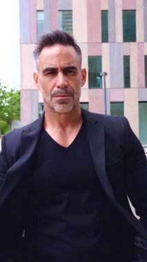 Siyah takım elbiseli şık bir adam ciddi ve kararlı bir ifadeyle ileri doğru yürüyor. Modern şehir geçmişi onun kendine güveni ve güçlü varlığını arttırır.. 