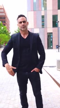 Siyah takım elbiseli şık bir işadamı şehir ortamında açık havada duruyor ve kararlı bir ifadeyle öne çıkıyor. Onun jesti liderlik, yön ve güven taşıyor.. 