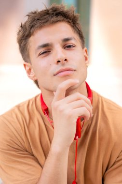 Düşünceli YouClose portresi, yüzünde derin bir ifade olan, elleri çenesinde, boynunda kırmızı kulaklıklar olan genç bir adam. Gelişigüzel şekilde şehir dışı ayarları