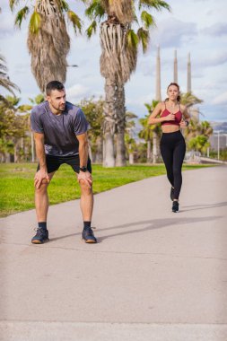 Bir kadın palmiye ağaçlarıyla parkta koşmaya devam ederken genç bir adam koşudan sonra soluklanıyor. Her ikisi de spor giyer ve kıyıya yakın güneşli bir günde dışarıda egzersiz yaparlar.. 