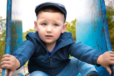  Şapkalı tatlı beyaz çocuk kaydırak kayarken gülümseyerek eğleniyor..