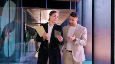  Resmi giyinmiş iki iş adamı, bir tablet kullanırken ve modern ofis koridorunda belgeleri tutarken, takım çalışmasını ve iletişimi sembolize ediyor.. 