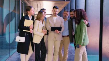 İş dünyasından profesyonellerden oluşan heyacanlı bir grup, modern ofis koridorundaki bir tablete bakarken resmi giyinmiş, tezahürat yapıyor ve başarıyı kutluyor, başarıyı ve takım çalışmasını simgeliyor.