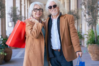 Gülümseyen Kafkasyalı son sınıf çifti alışveriş torbaları taşıyor ve şık bir günün tadını çıkarıyor. Doğal ışığı olan zarif bir şehir ortamında modern yaşam tarzı, moda ve eğlence kavramı.