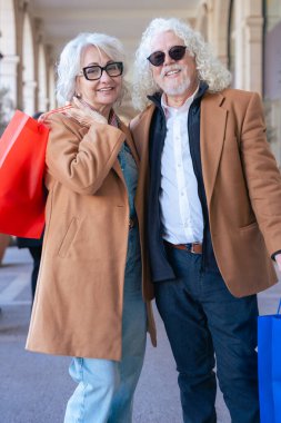 Gülümseyen Kafkasyalı son sınıf çifti alışveriş torbaları taşıyor ve şık bir günün tadını çıkarıyor. Doğal ışığı olan zarif bir şehir ortamında modern yaşam tarzı, moda ve eğlence kavramı.