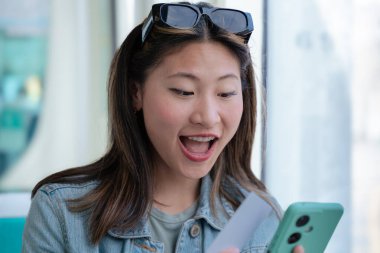 Mutlu genç Çinli kadın tramvayda oturuyor ve akıllı telefonuyla sosyal medyayı kontrol ederken gülümsüyor. Şehir toplu taşıma sahnesi. Yaşam tarzı, teknoloji ve seyahat için ideal..