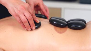 Sıcak taş masajının yakın görüntüsü, rahatlatıcı bir terapi seansı sırasında sırtüstü uzanmış siyah taşlar. Spa, sağlık, şifa ve alternatif sağlık kavramları için mükemmel.. 