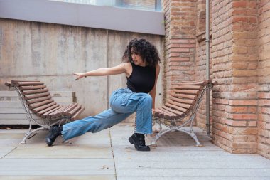 Afro-Amerikalı bir kadın şehir ortamında banklar arasında yaratıcı bir pozda dans ediyor. Günlük kıyafetler giyiyor ve denge, güç ve ifade gösteriyor. Hareket, sanat ve özgürlük kavramı. 