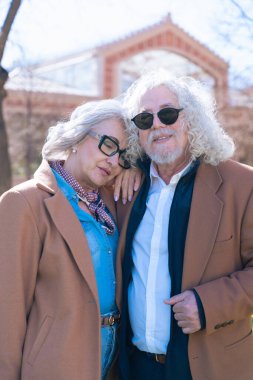 Kafkasyalı yaşlı bir çift güneşli bir parkta dikiliyor. Kadın başını erkeğin omzuna yaslıyor, ikisi de kahverengi ceketler ve gözlük takıyor, sessiz ve sevgi dolu bir anı paylaşıyor. 